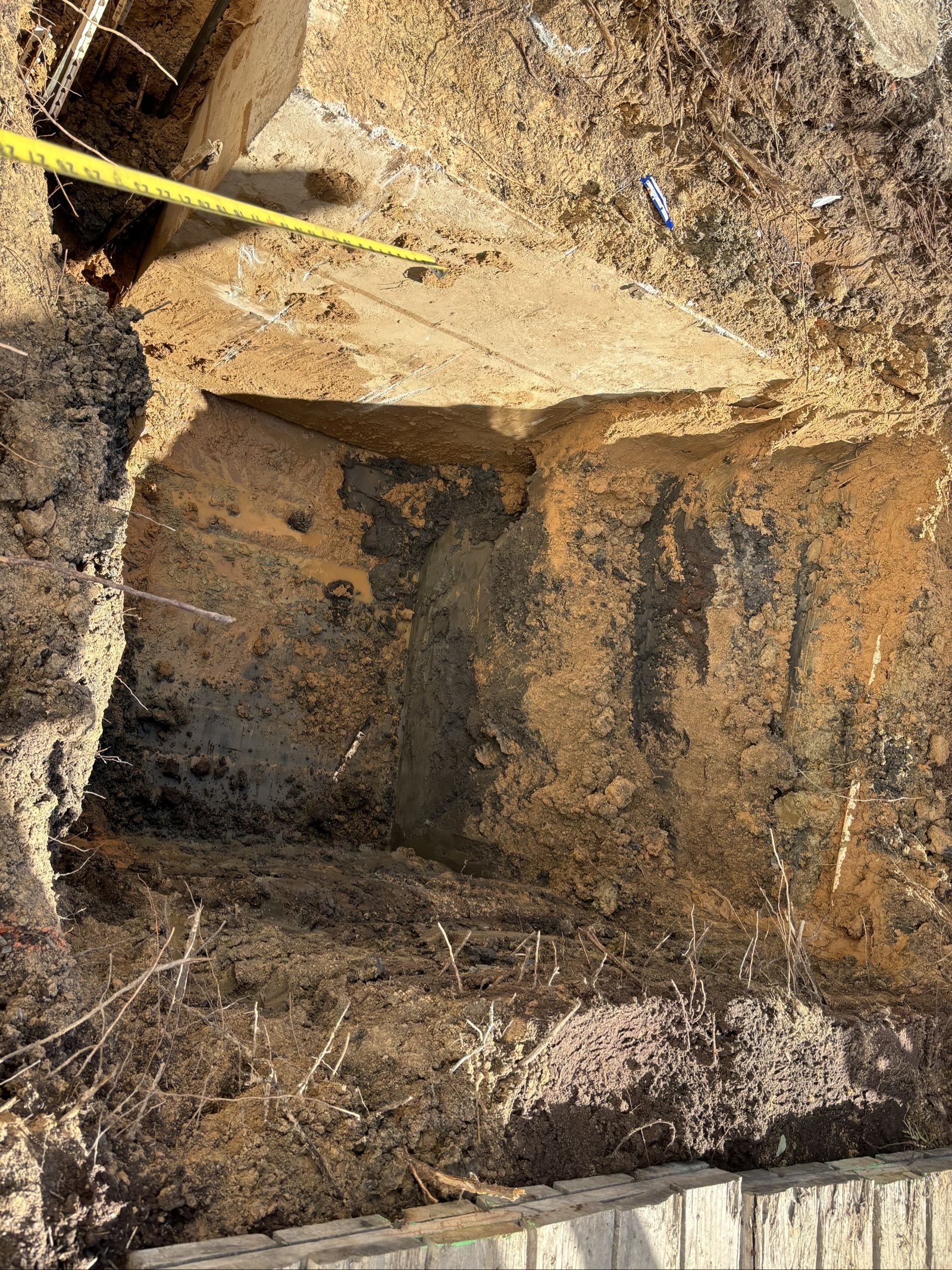 Septic installation excavation with a measuring tape showing soil depth before the tank is set