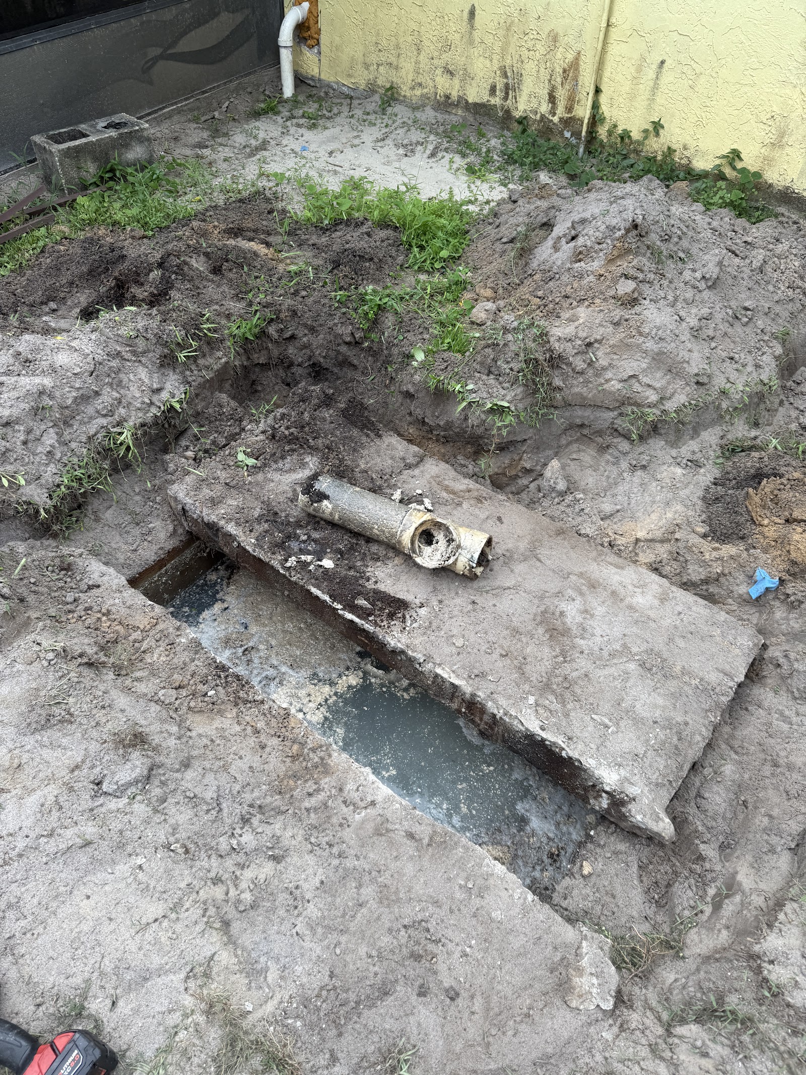 Excavated residential septic line showing a deteriorated pipe repair with standing water