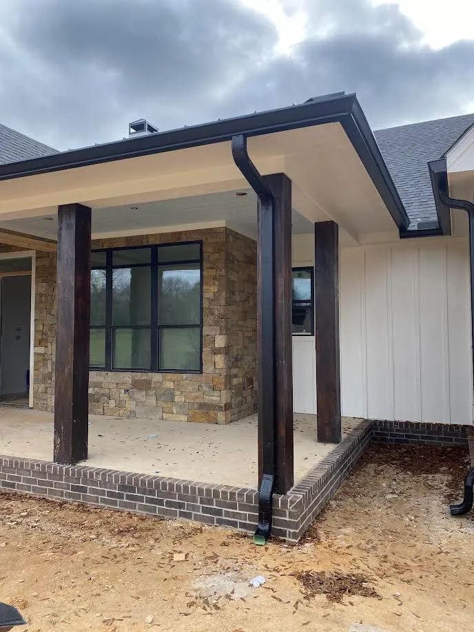 Covered front porch of a new East Texas home with stone base and black seamless gutter and downspout
