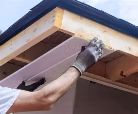 Crew member replacing rotten fascia board under a roof eave before new gutter installation