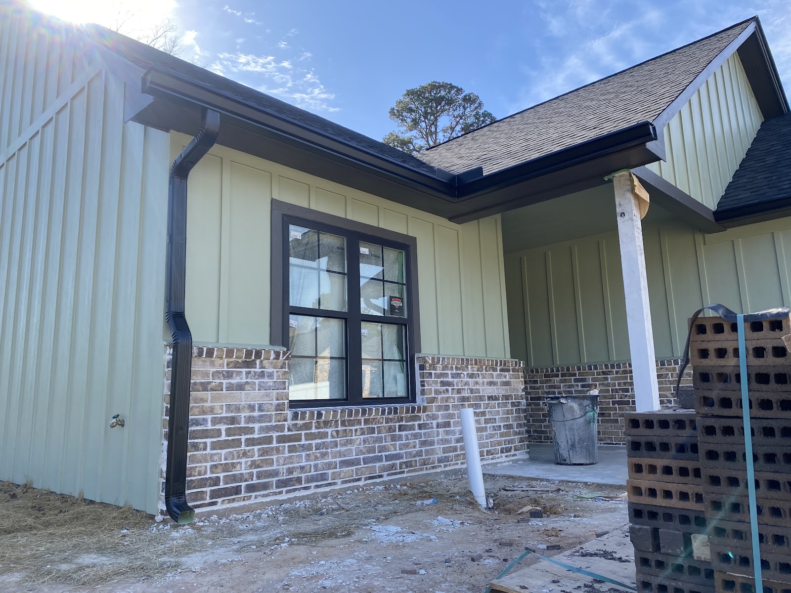 New black seamless gutter and downspout installed on a brick and sage siding home in Nacogdoches