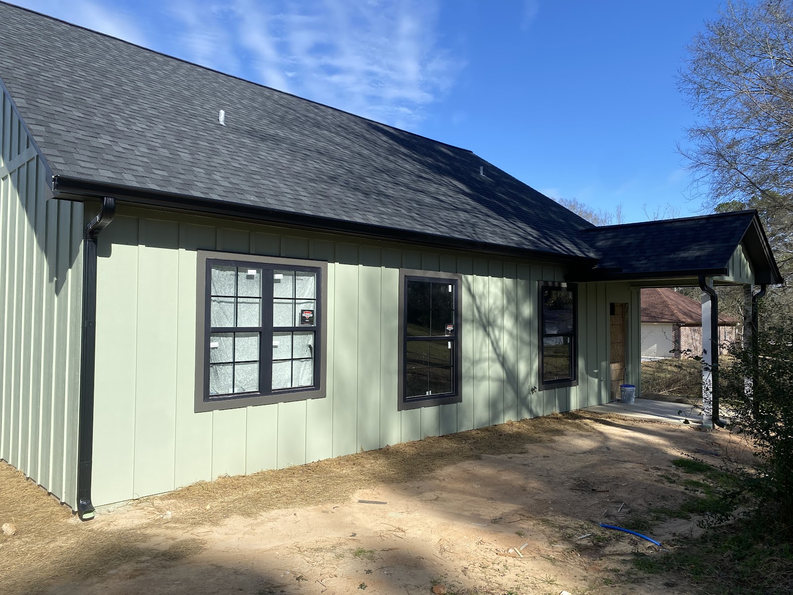Black seamless gutters installed on a sage green board-and-batten home in East Texas