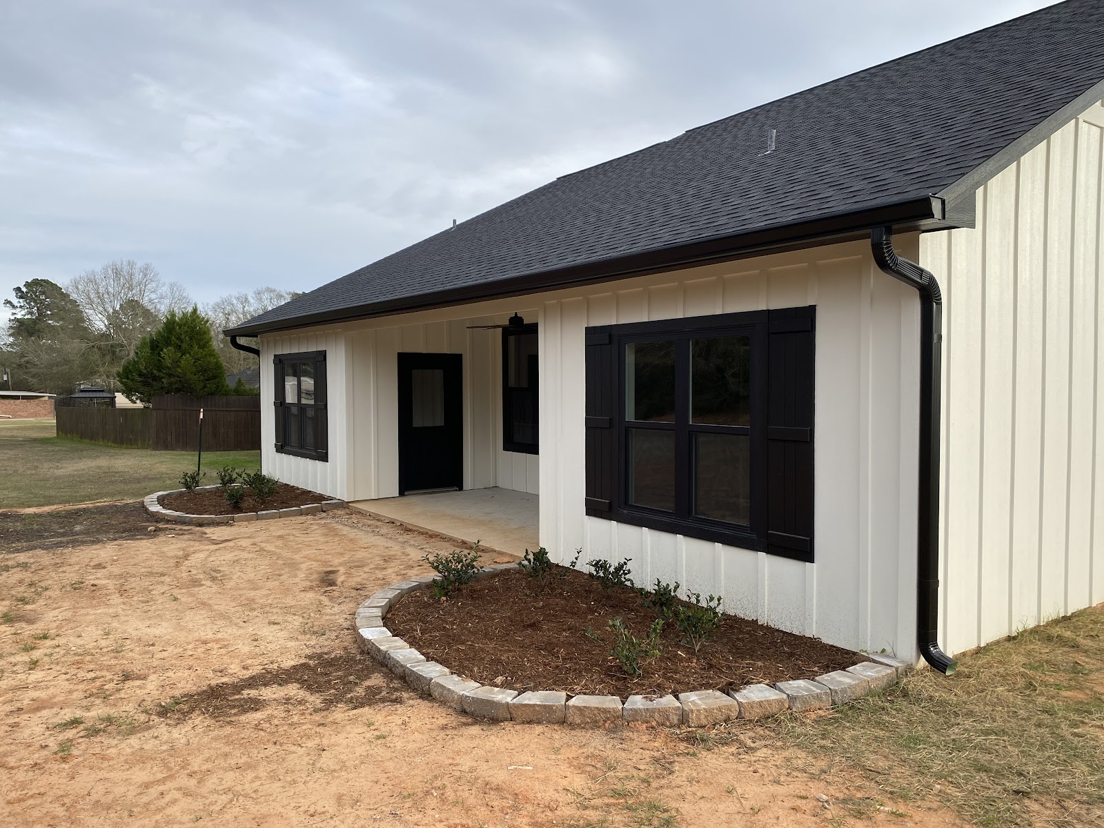 White board-and-batten Nacogdoches home with black seamless gutters, downspout and fresh landscaping