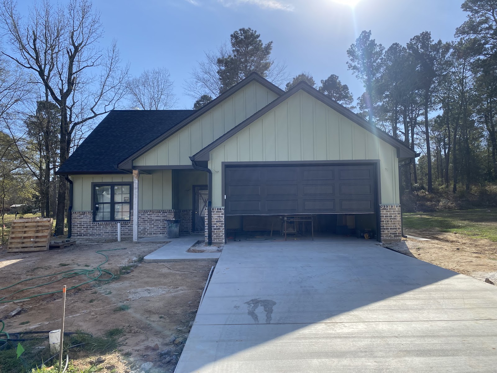 Single-story East Texas home with asphalt shingle roof, board-and-batten siding and brick base