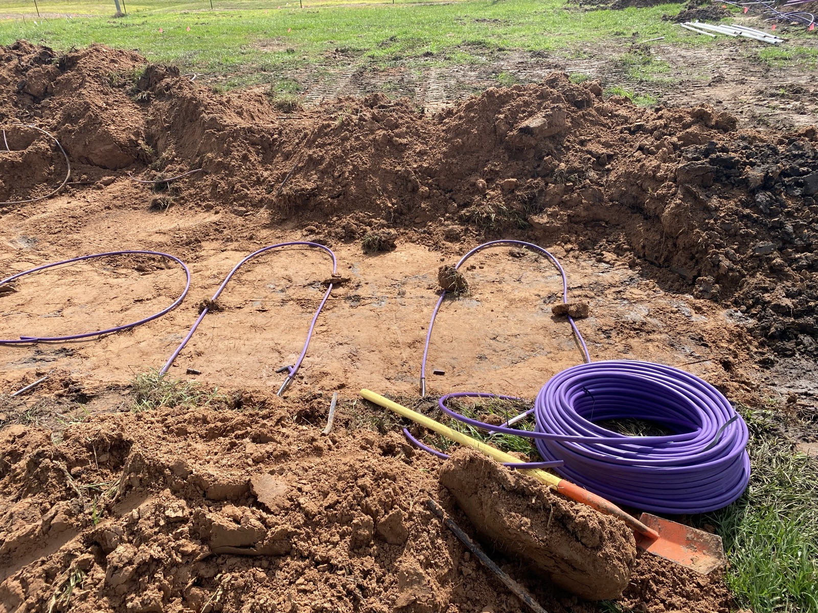 Purple electrical conduit laid out during underground installation on residential jobsite with dirt piles.
