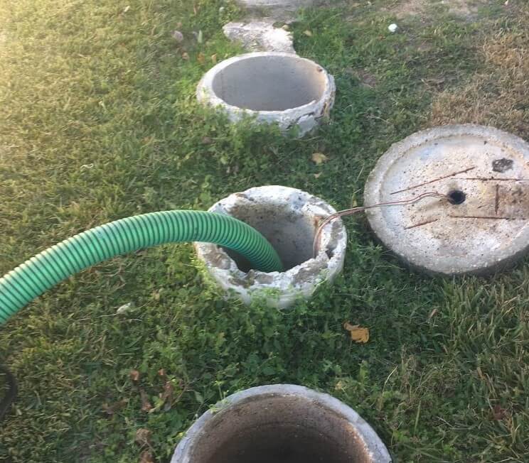 Septic tank system with green pump hose connected to concrete access ports in grass yard.