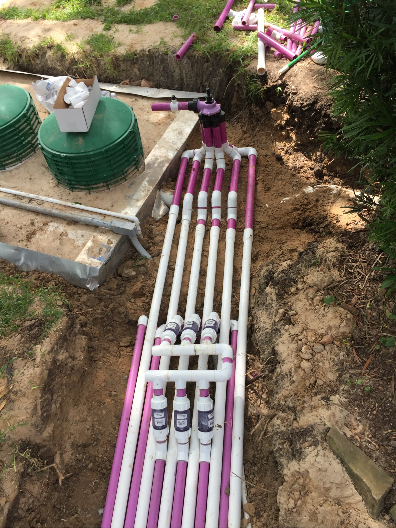 Underground septic system installation with purple and white PVC pipes in residential trench
