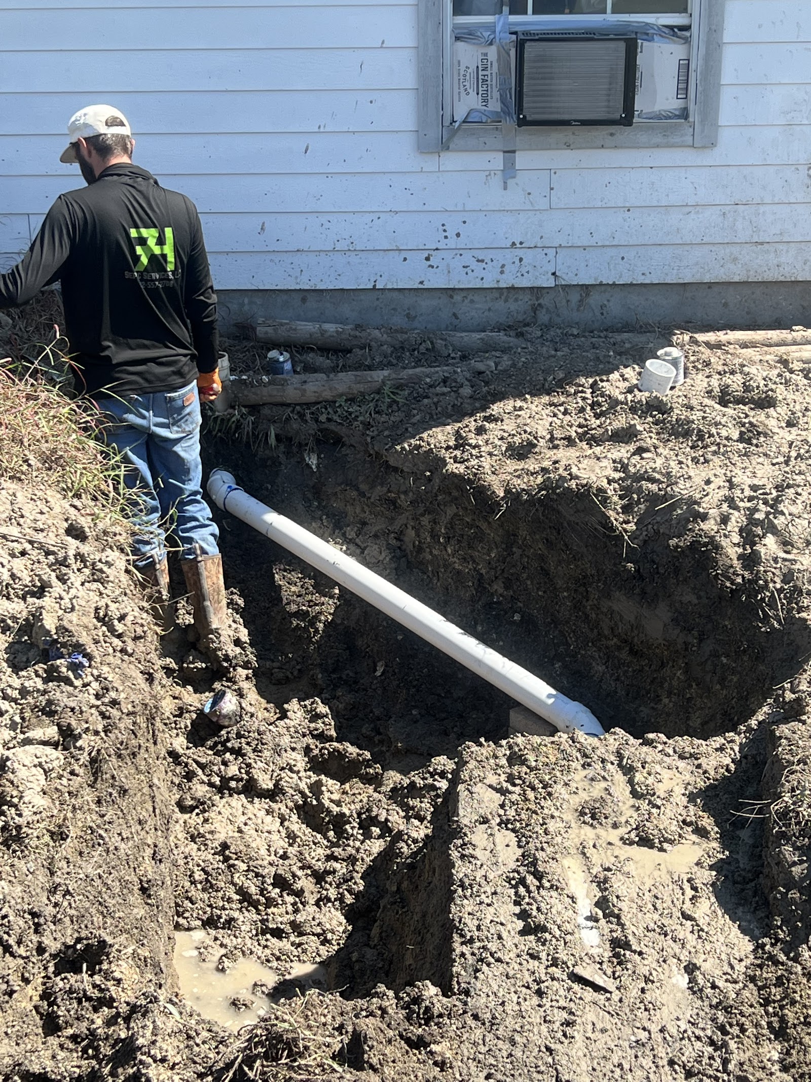 Technician installing white drainage pipe in residential foundation excavation trench