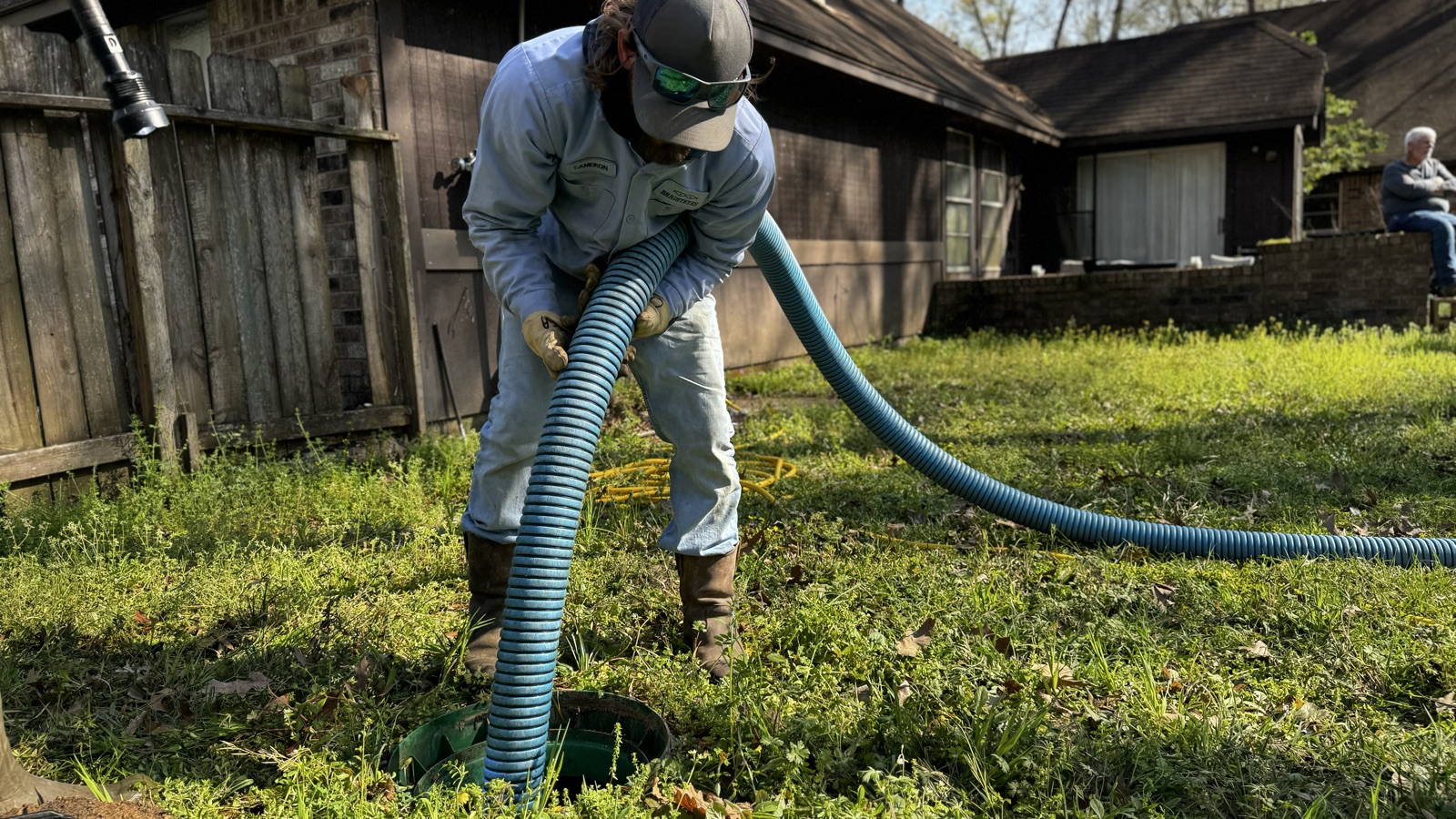 Technician in blue uniform pumping septic tank with hose in residential yard
