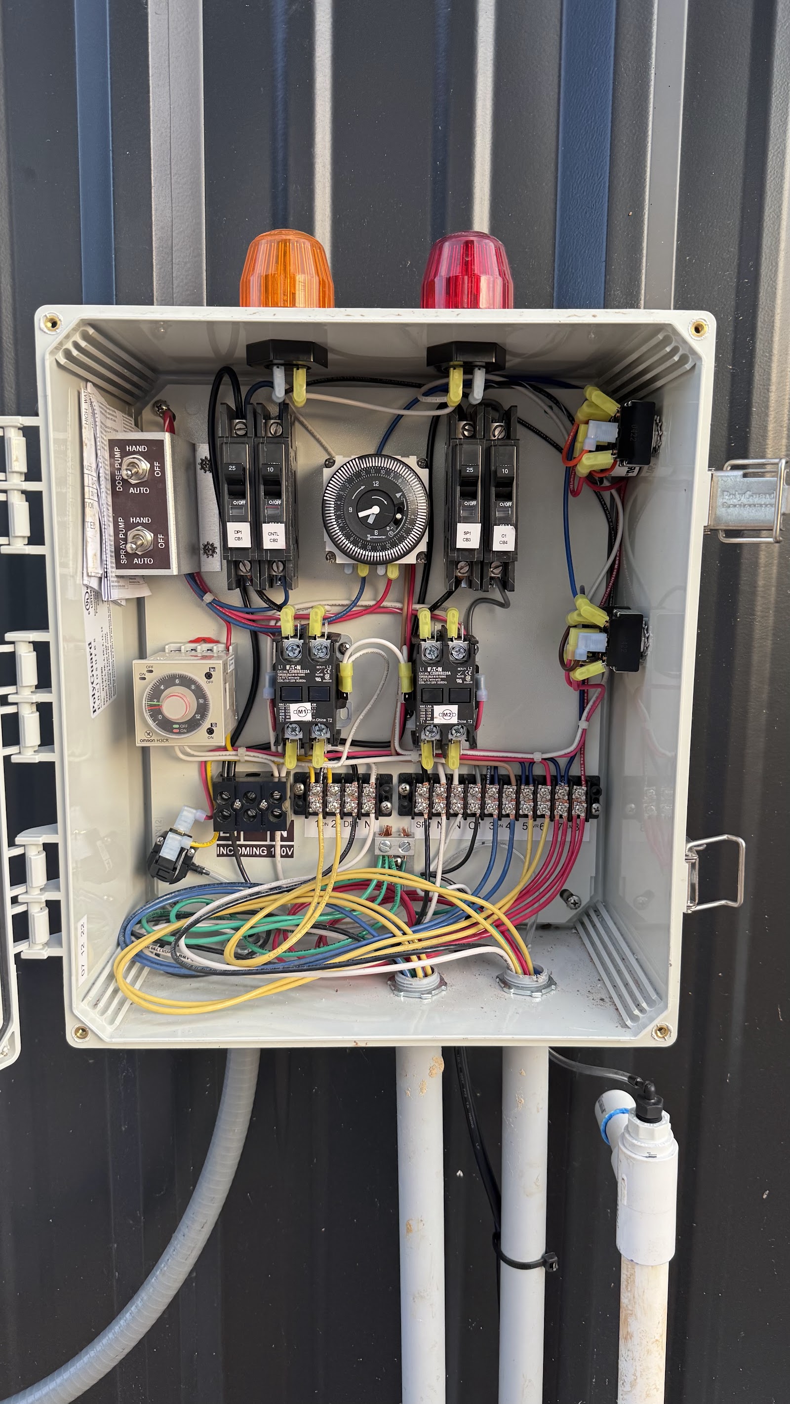 Open septic system electrical control panel with timers, breakers and indicator lights on a metal wall