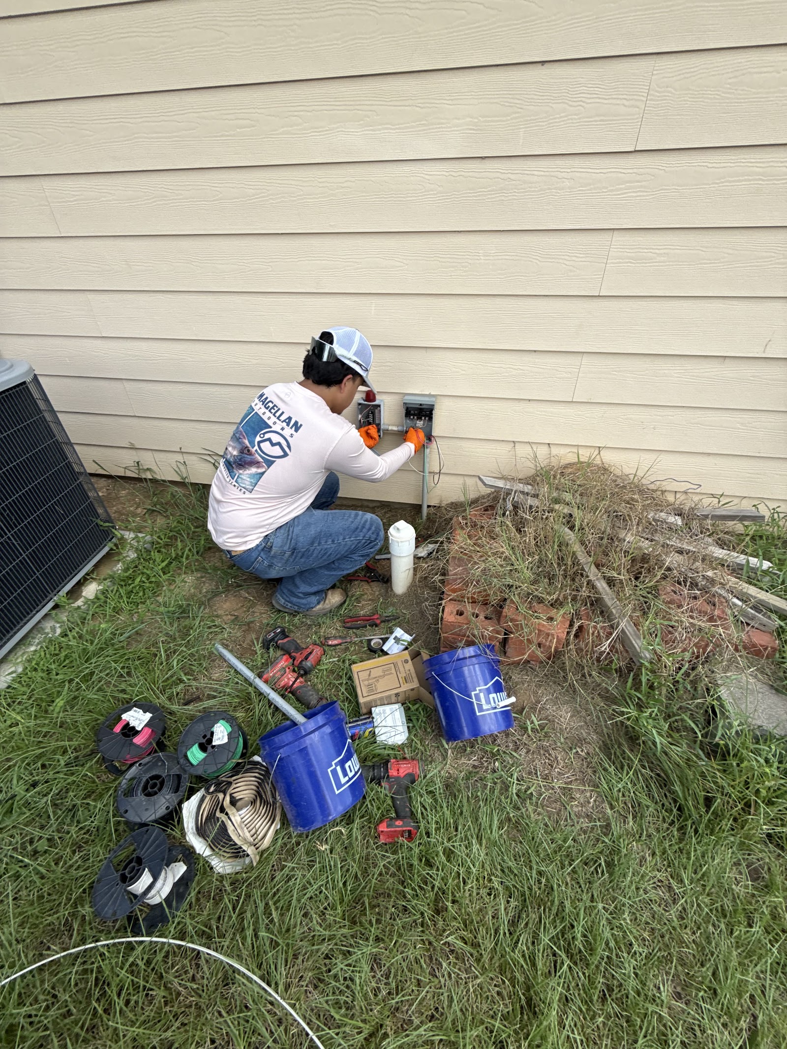 Septic technician wiring an electrical box on a house exterior beside tools and wire spools