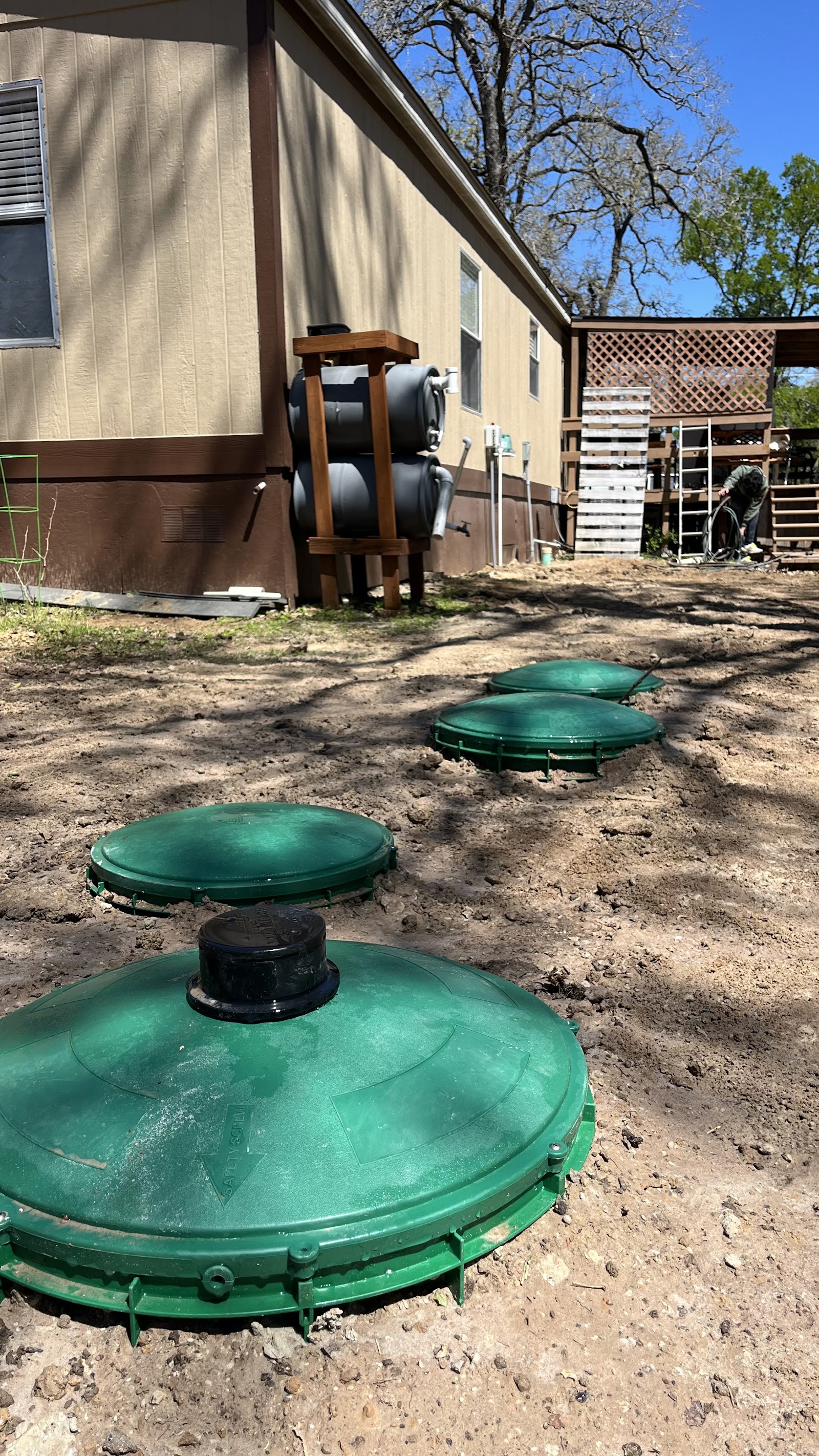 Four green septic tank access lids installed at grade beside a mobile home in a residential yard