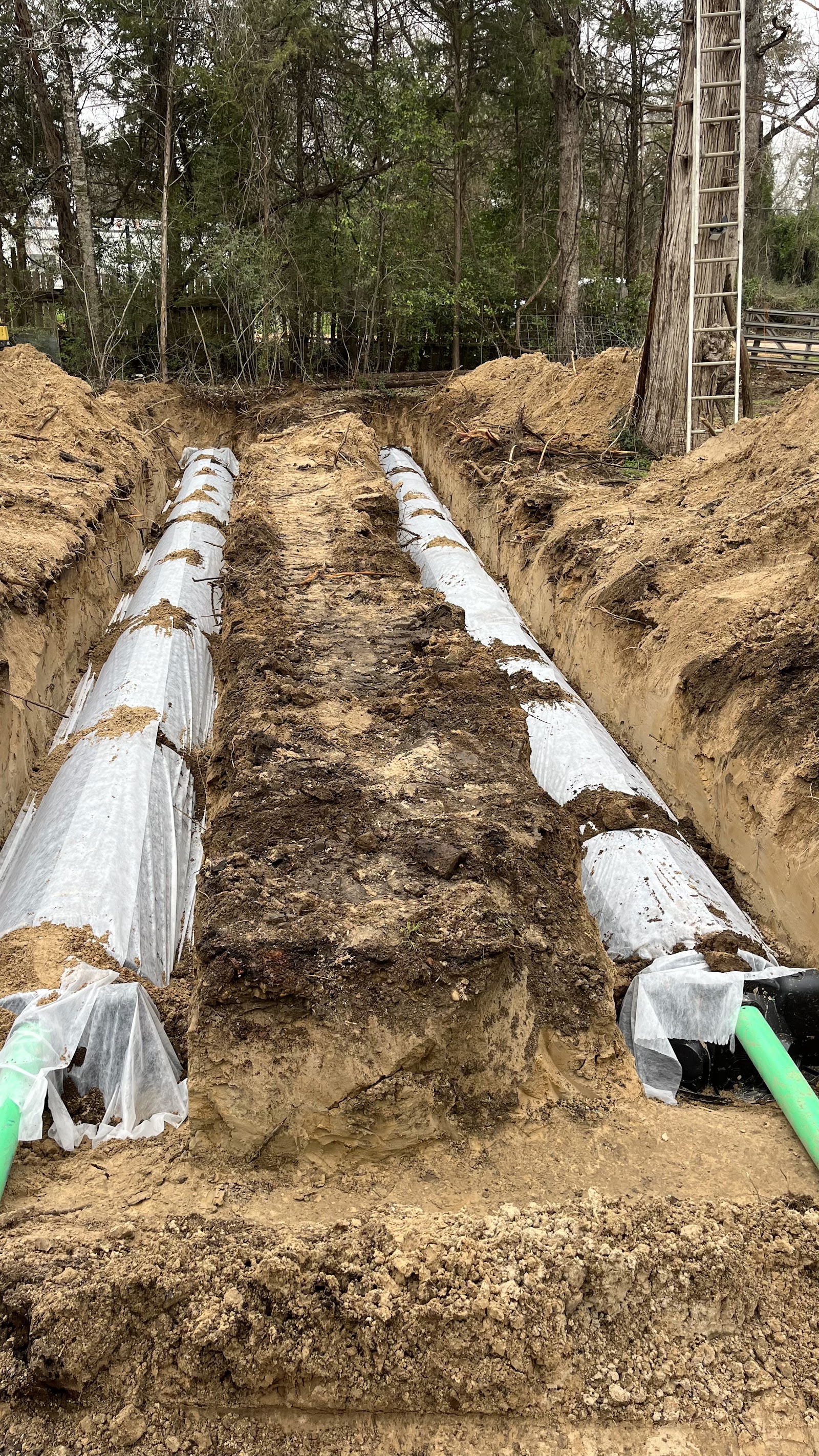 New septic drainfield install: excavated trench with geotextile-wrapped drain lines and green pipes