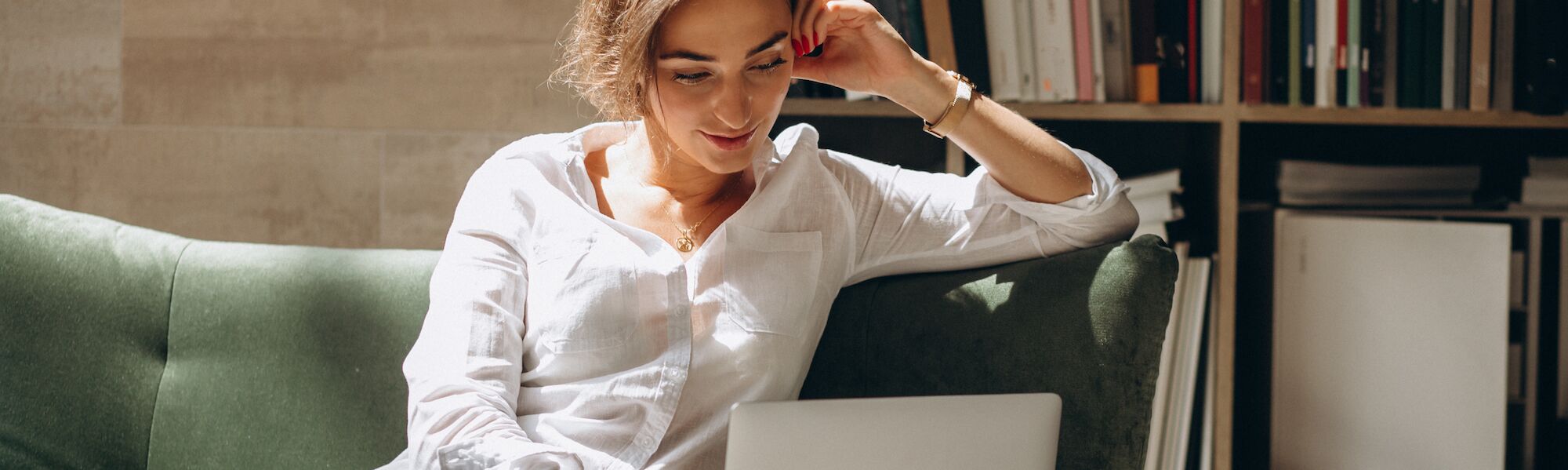 Professional woman in white shirt working on laptop while seated on green couch