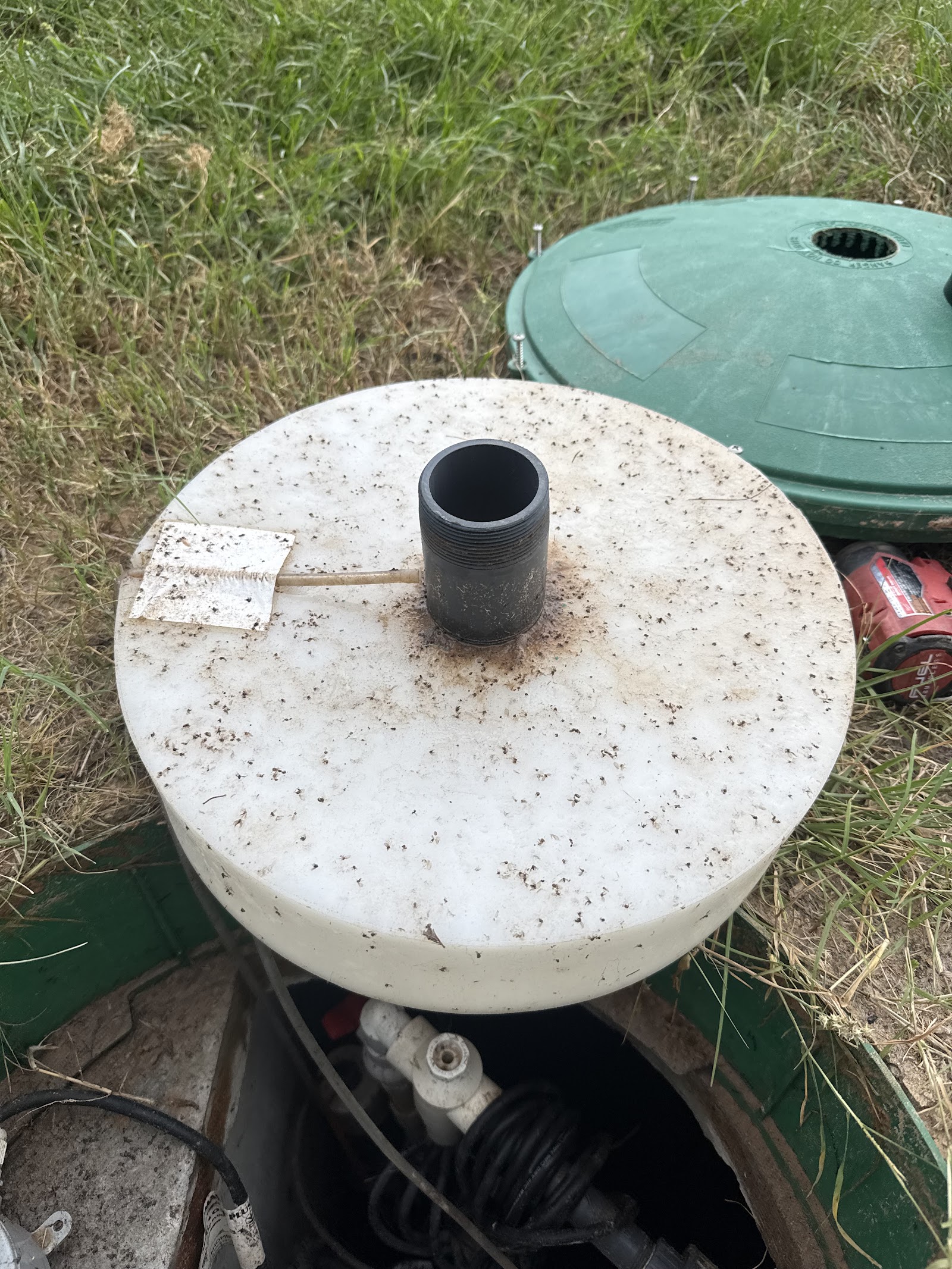 White aerobic septic tank lid with black vent pipe in a grass yard, ready for a maintenance inspection