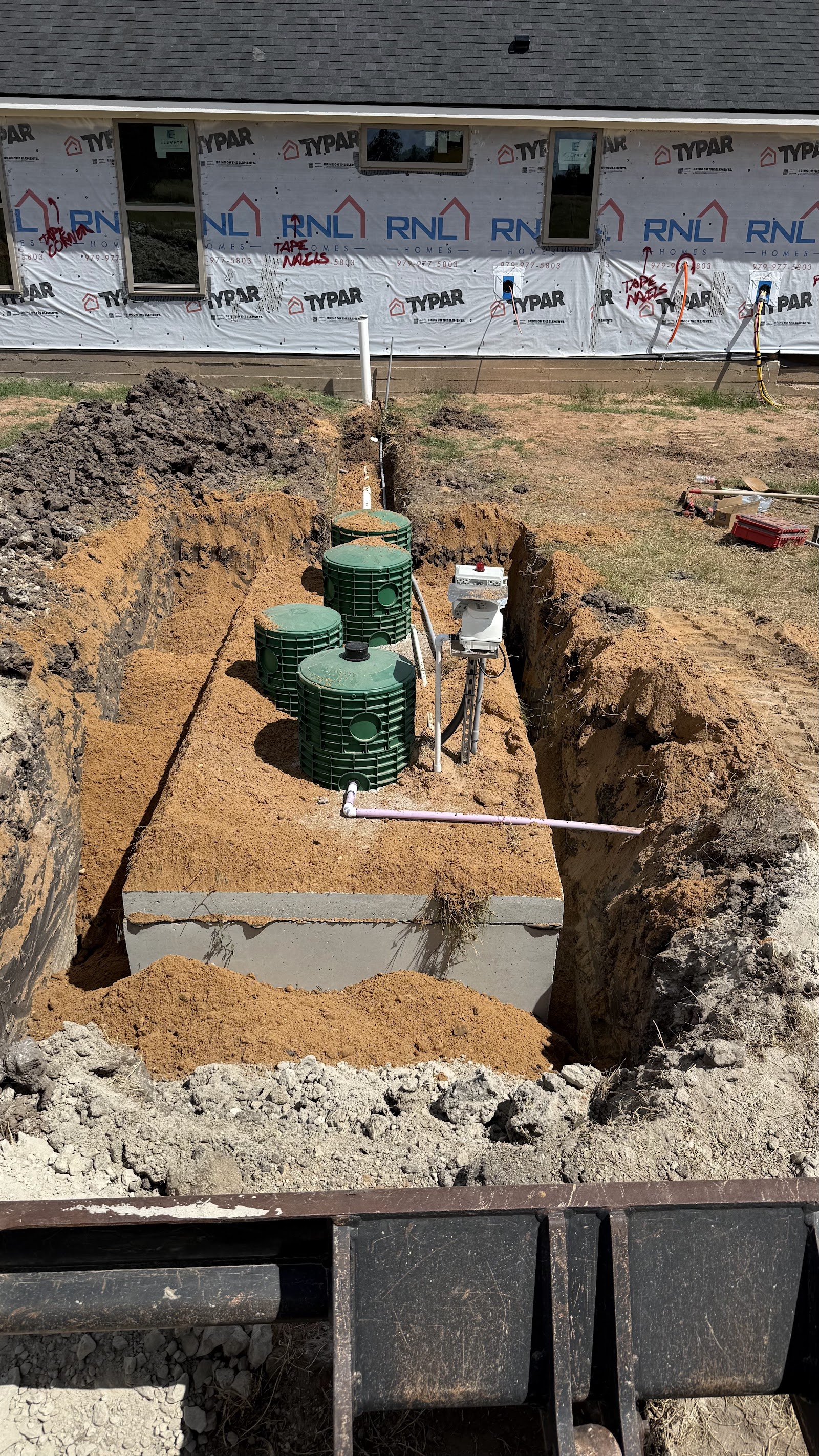 New aerobic septic tank lids and pipe in an excavated trench beside a house under construction