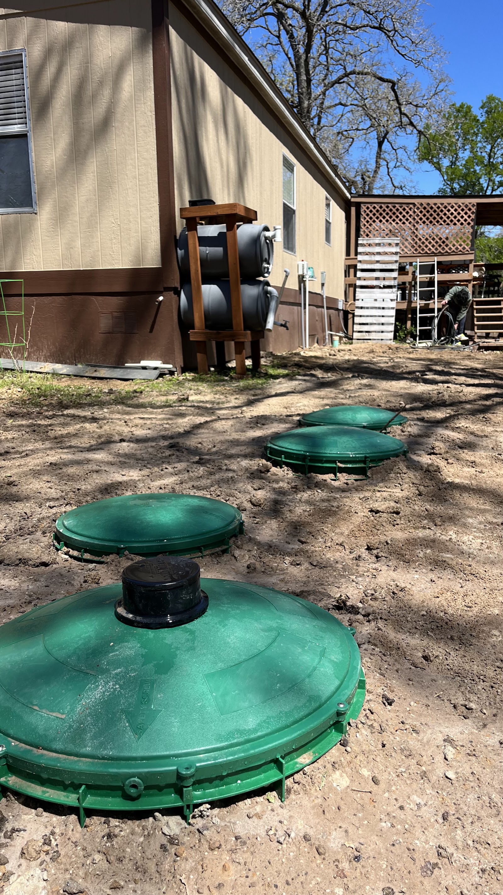 Green aerobic septic tank access lids in a yard beside a tan mobile home