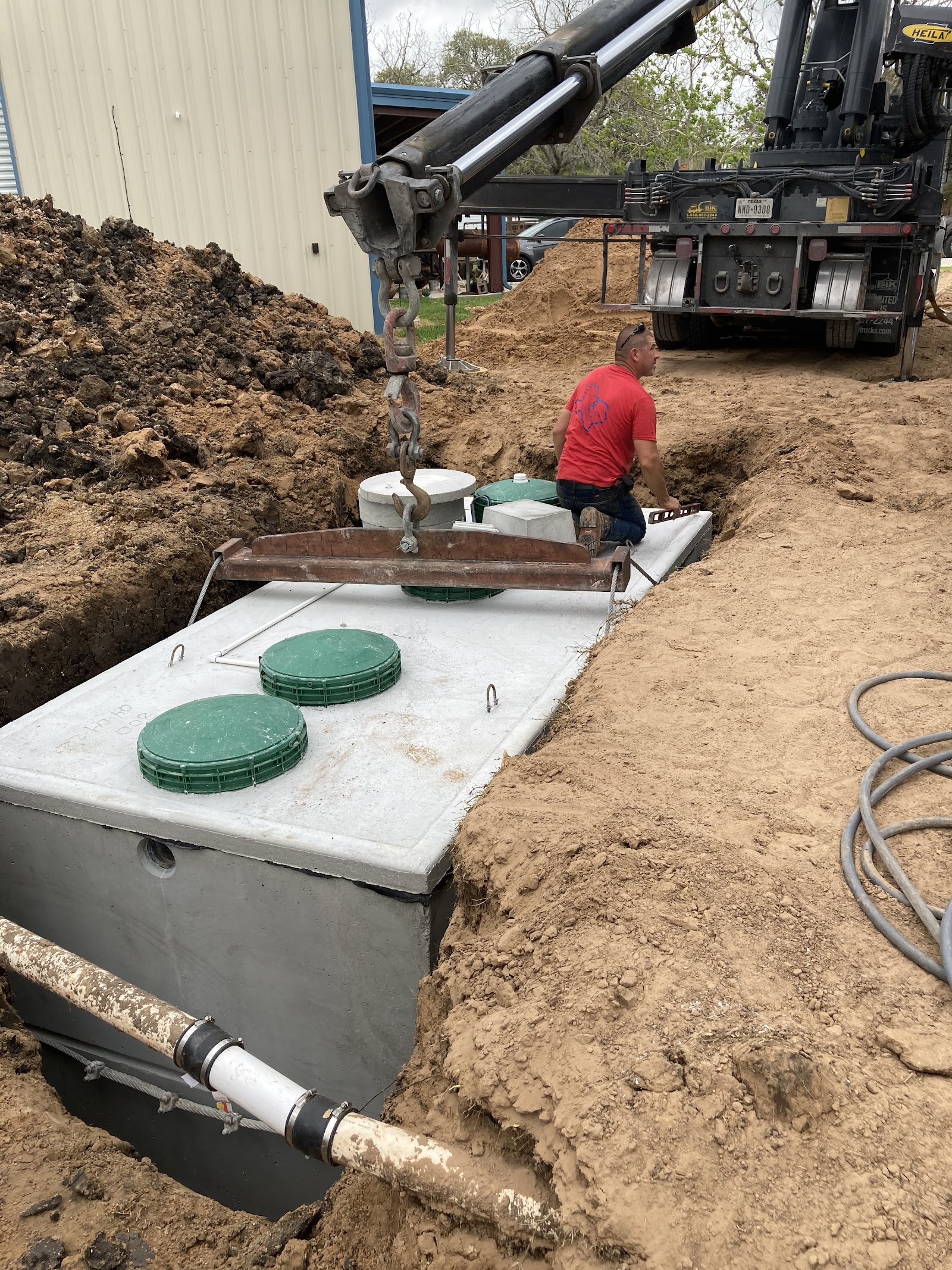 Septic tank installation in progress with crane lowering concrete tank into ground excavation pit