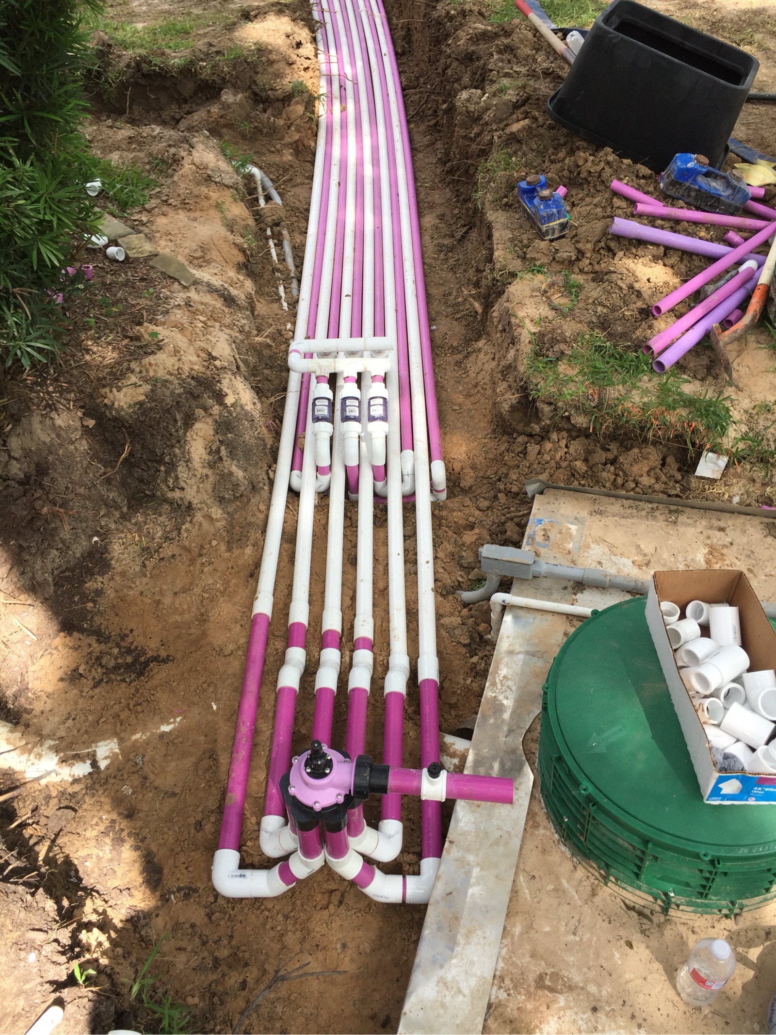 Underground plumbing installation with pink and white PVC pipes laid in trench during residential construction