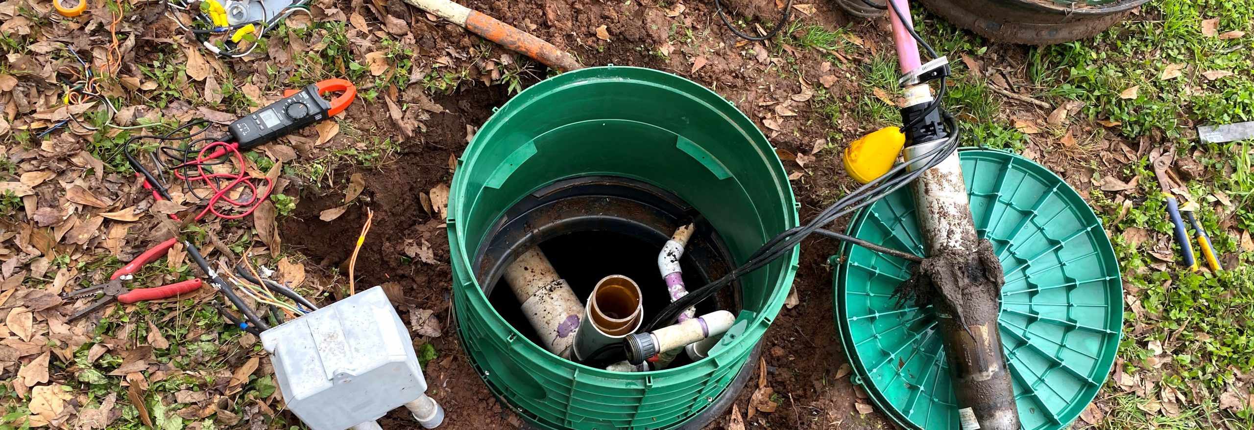 Technician inspecting underground septic tank with piping and electrical connections visible