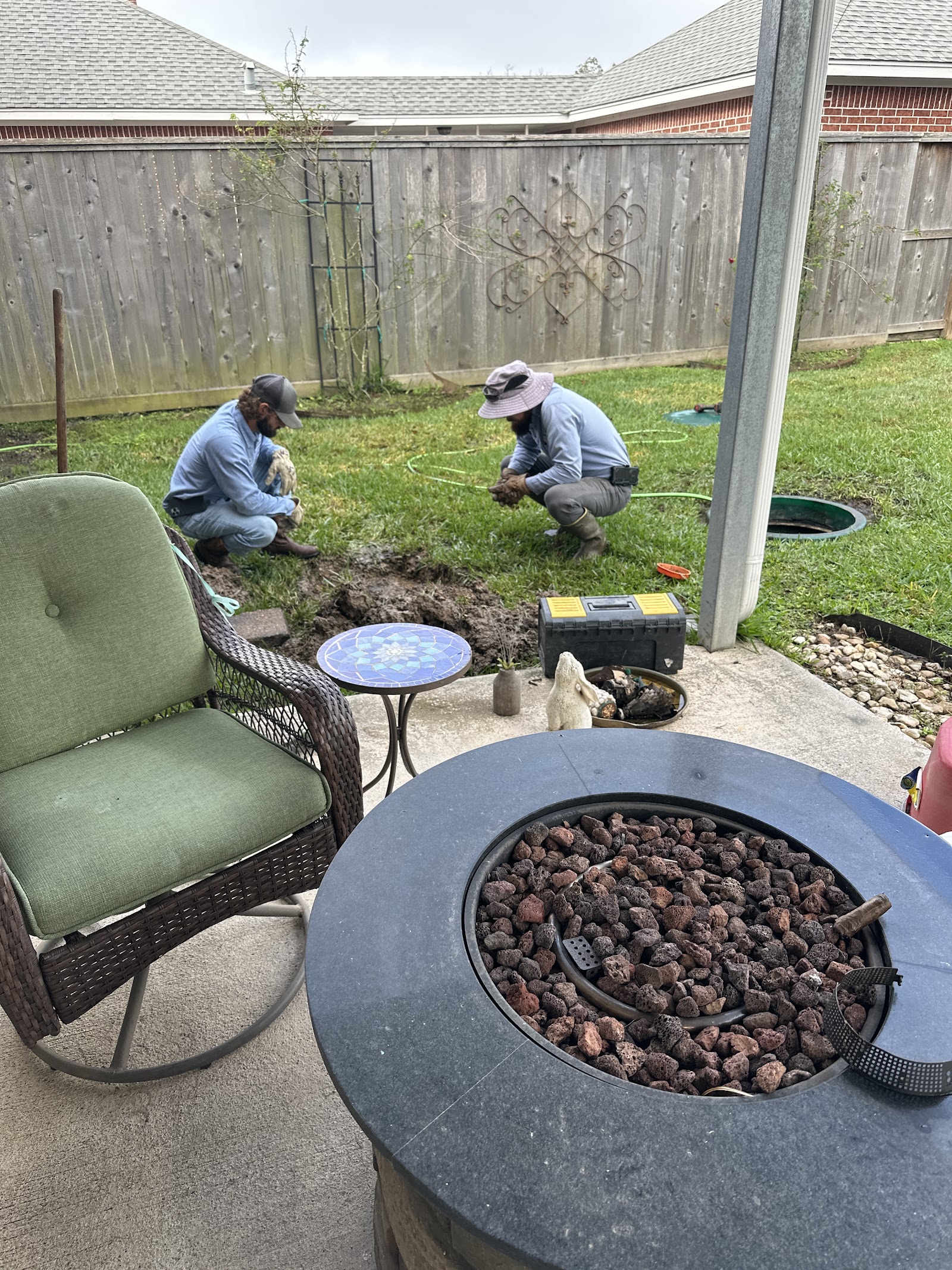 Two technicians inspecting and discussing yard drainage work near fire pit in residential backyard