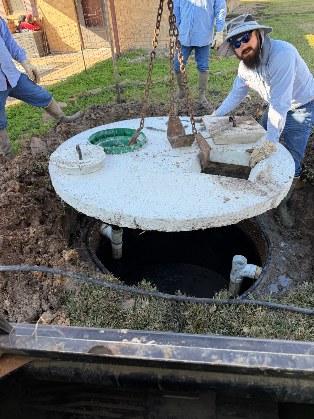 Technician inspecting opened septic tank system with chain hoist during maintenance work